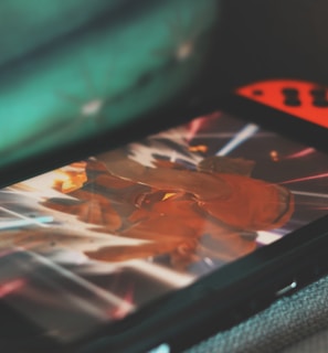 A portable gaming console with neon red and blue controllers displays an action-packed scene from a video game. The screen is focused on a character surrounded by bright, dynamic light effects.