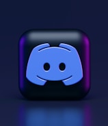 A 3D-style block with a blue logo in the center, set against a dark background. The logo resembles a game controller with two rounded edges and two circles on the front. The block has a subtle gradient, transitioning from dark to purple on its sides.