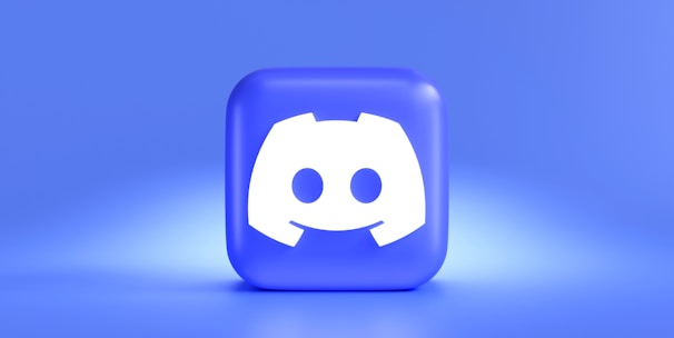 A three-dimensional blue cube featuring a white, stylized gaming controller symbol associated with a popular communication platform, set against a gradient blue background.