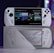 A handheld gaming console with a screen displaying a game library menu is placed on top of its packaging. The console features various buttons, a joystick, and a circular light around the left joystick. The background is blurred with purple, yellow, and blue tones.
